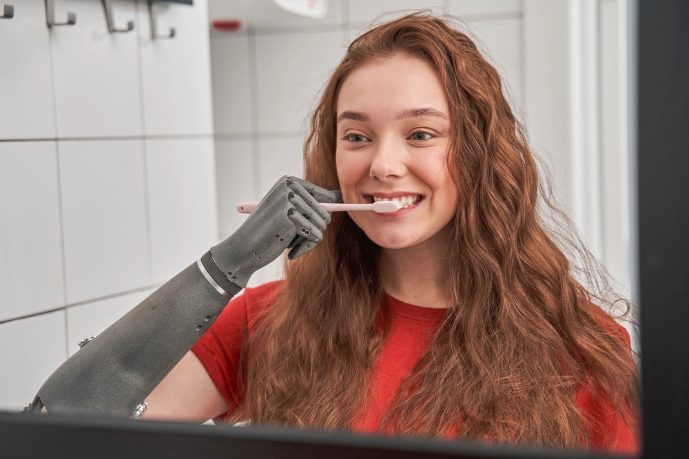 women brushing her teeth with prosthetic hand and looking in mirror