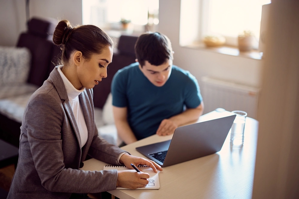 carer helping disabled boy fill an online form on laptop