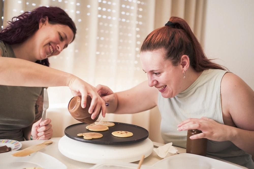 carer helping disabled women in cooking and making pancakes